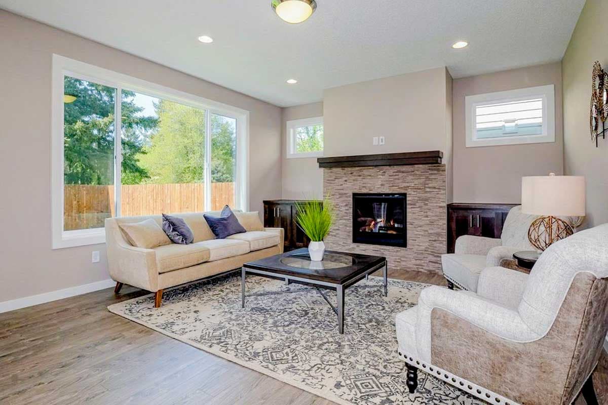 Living room with stone fireplace, large picture window, neutral sofa and chairs, and patterned area rug.
