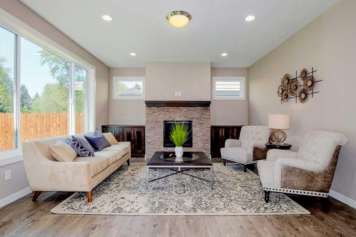 Living room with fireplace, sofa, two armchairs, large window, and wood paneling.