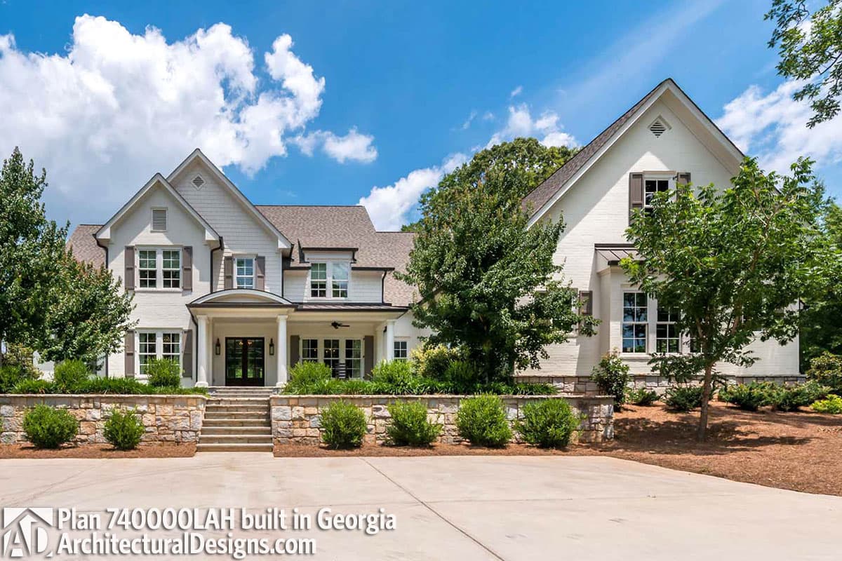 House plan exterior with covered entrance, multiple gables, dormers, and stone retaining wall.