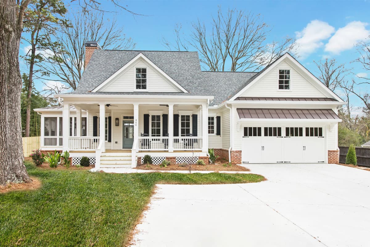 House plan exterior featuring a two-story farmhouse style with a front porch, gables, and an attached garage with carriage doors.