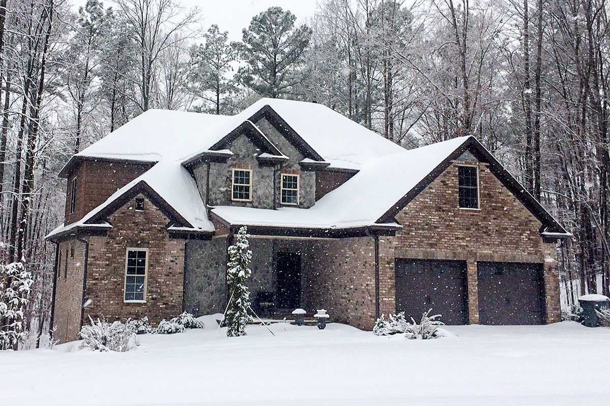 House plan exterior: Two-story brick and stone home with covered porch, gables, dormers, and a three-car side-entry garage.