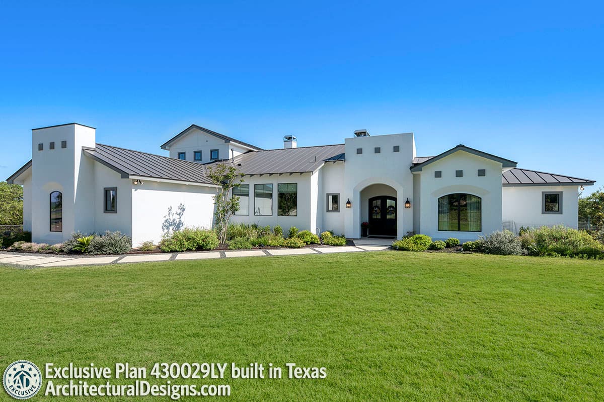 House plan exterior. Two-story, stucco exterior with a low-slope roof, arched entryway, and a tower element. Featuring multiple gables.