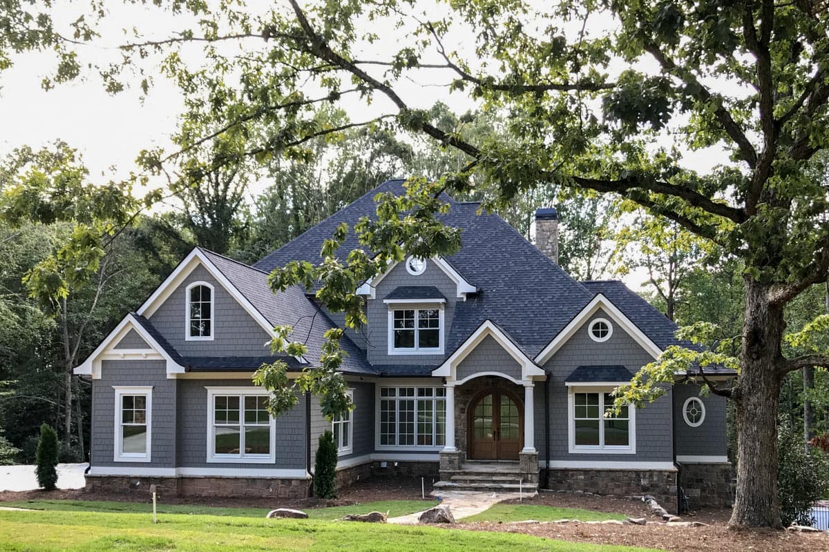 Craftsman house plan exterior, two stories, with arched double doors, dormers, and stone foundation.