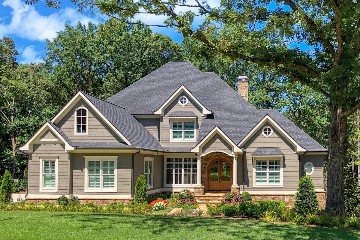 House plan exterior: Craftsman style, two stories, prominent gables, arched entry with double doors, stone base, and dormer windows.