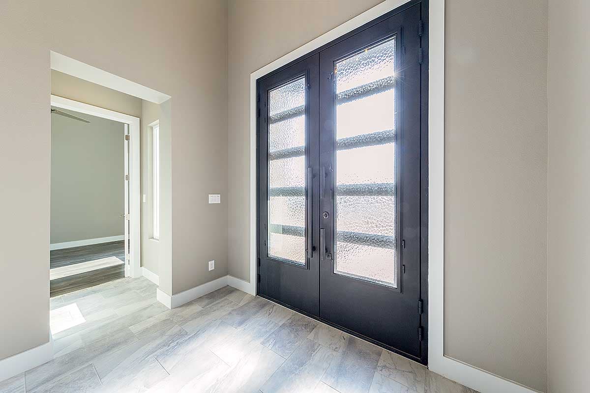 Double entry doors with frosted glass panels leading to a hallway with light wood-look tile flooring.