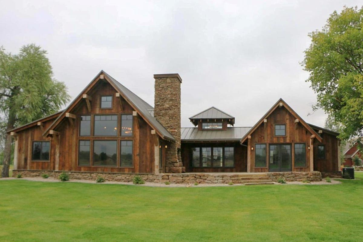 Rustic timber exterior house plan with large windows, stone chimney, and metal rooflines.