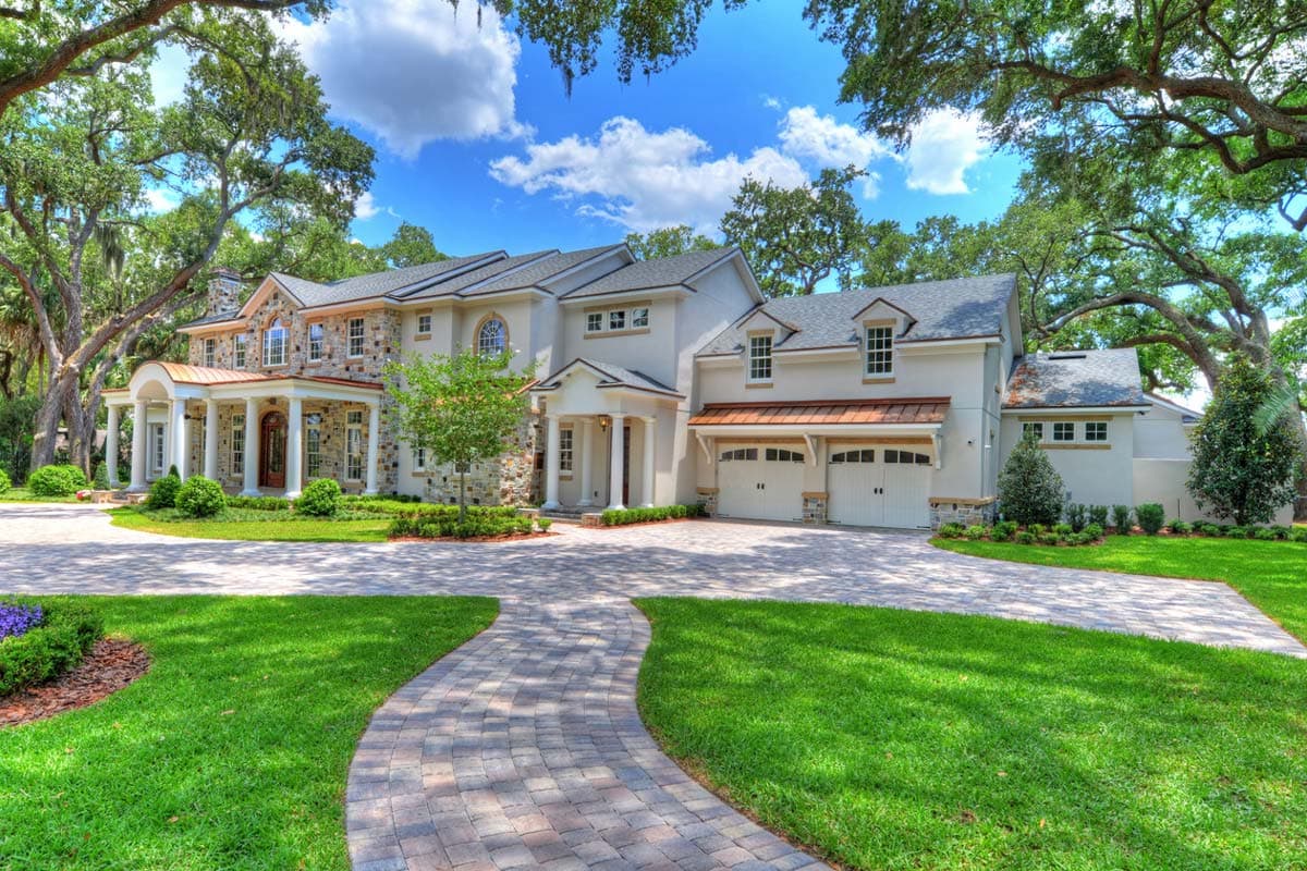 House plan exterior. Two-story, stucco facade with stone accents. Features include a portico, dormers, and a three-car garage.