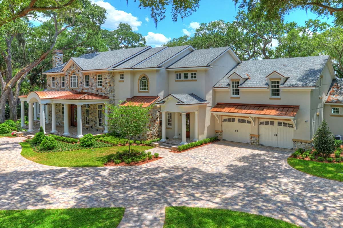 House plan exterior: Two-story home with stone accents, a curved covered porch with columns, and a three-car garage.