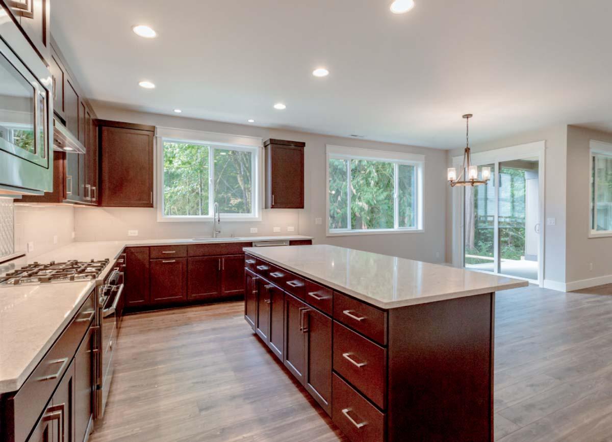 Kitchen with dark wood cabinets, large island, stainless steel appliances, and natural light from windows.