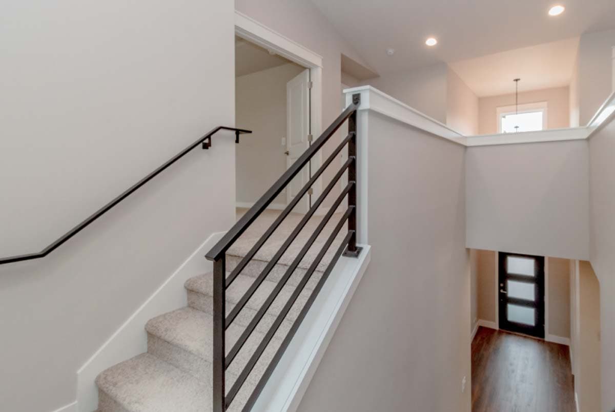 Interior view of staircase with modern horizontal bar railing and carpeted steps leading to a hallway with a glass-paneled door.