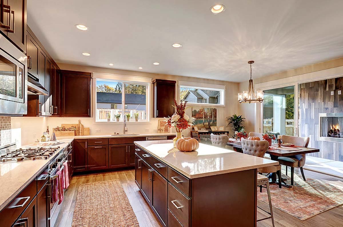 Kitchen and dining area with island, fireplace, and large windows. House plan interior.