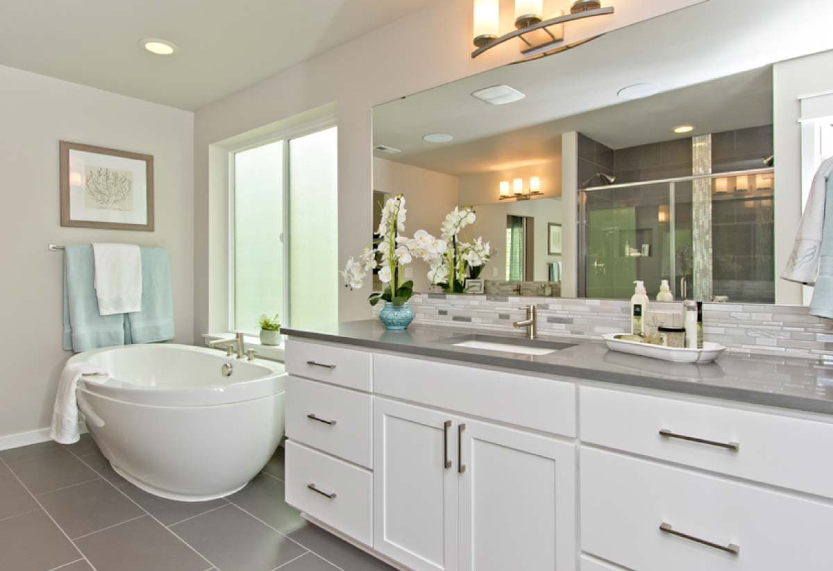 Modern bathroom with soaking tub, dual vanity, large mirror reflecting shower area, and window.