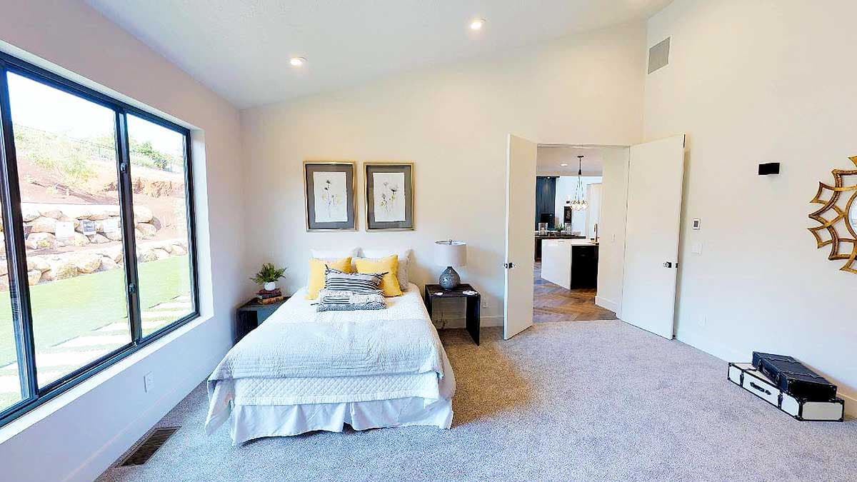 Bedroom with vaulted ceiling, large window, and view into kitchen with island.