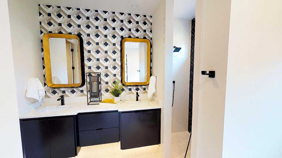 Bathroom vanity with double sinks, geometric wallpaper, black cabinets, and tiled shower.