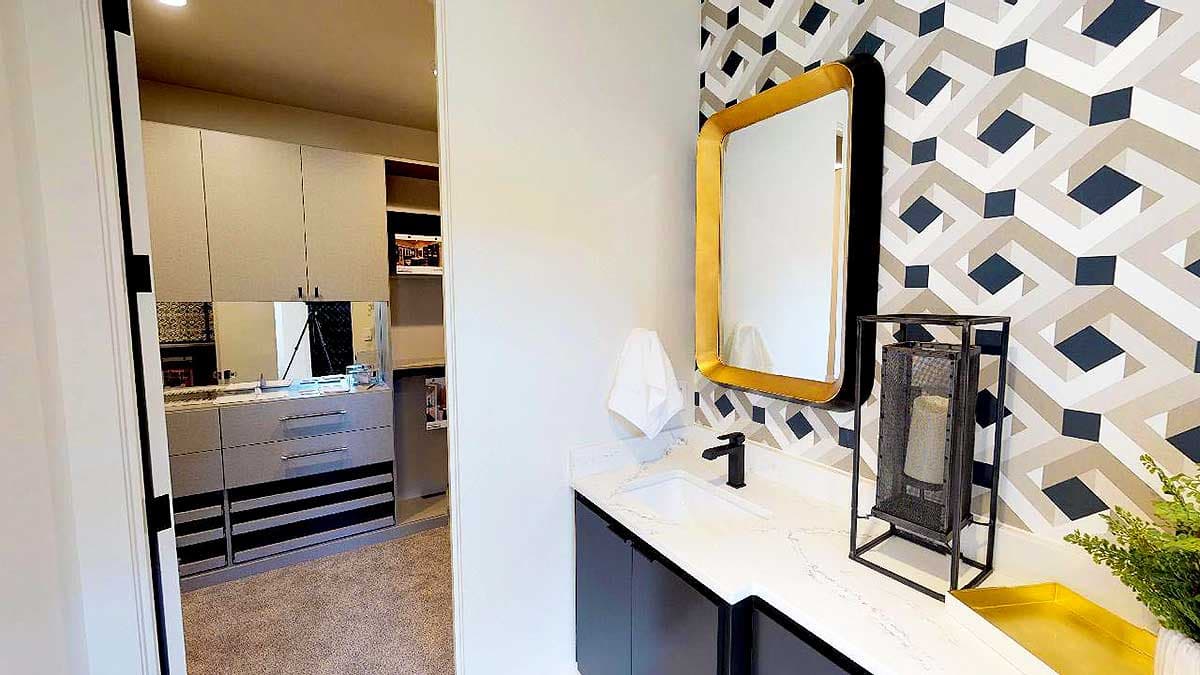Bathroom with geometric wallpaper, vanity, sink, gold-framed mirror, and walk-in closet with storage.