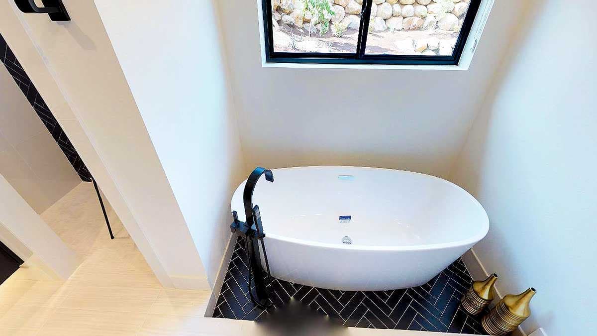 Freestanding oval bathtub with black floor-mounted faucet and herringbone tile surround.
