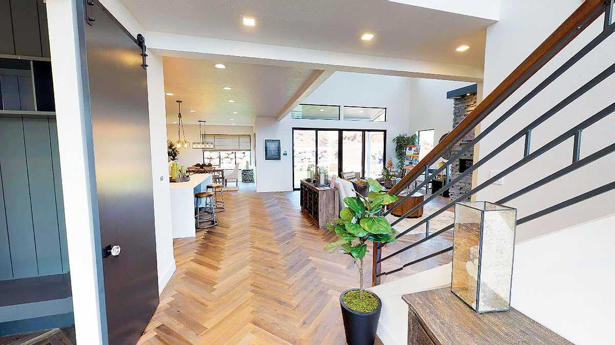 Open concept interior with herringbone wood floors, kitchen island, large windows, and a metal barn door.