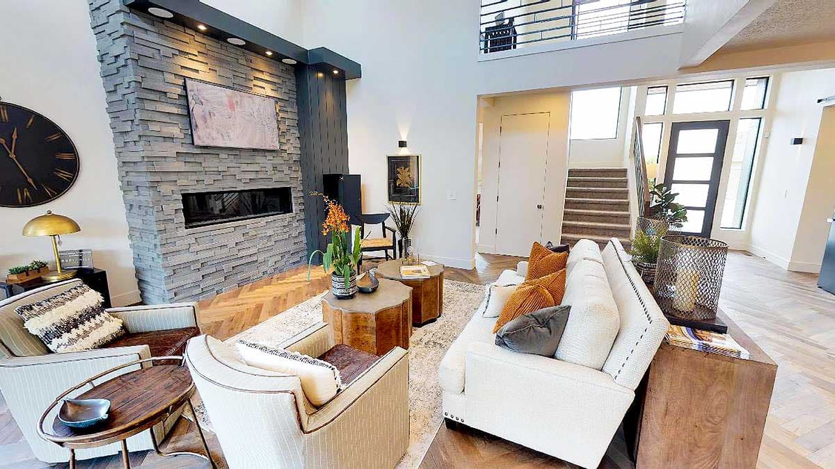 Great room with stacked stone fireplace, vaulted ceiling, open staircase, and modern entryway.