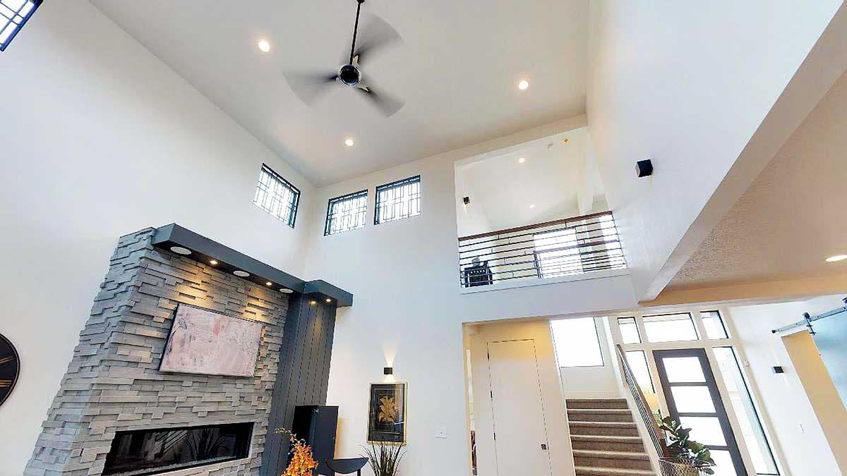 Interior view of a great room with a multi-story stone fireplace, vaulted ceiling, ceiling fan, and loft overlook.