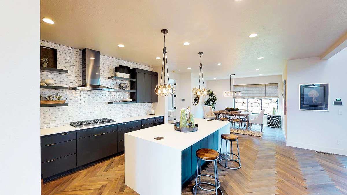 Kitchen interior with white subway tile backsplash, dark cabinets, large island with seating, and open dining area beyond.