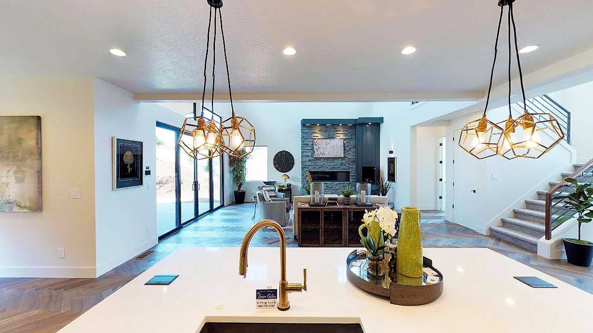 Interior view showing a modern open-concept living space with a kitchen island, stone fireplace, and a staircase.