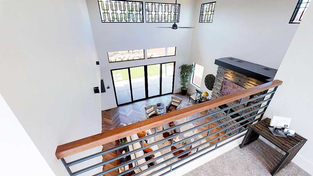Interior view of a modern great room with vaulted ceiling, stone fireplace, herringbone wood floors, and large sliding glass doors.
