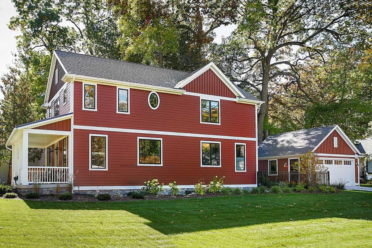 Two-story house plan exterior with red siding, gables, dormers, wraparound porch, and attached garage.