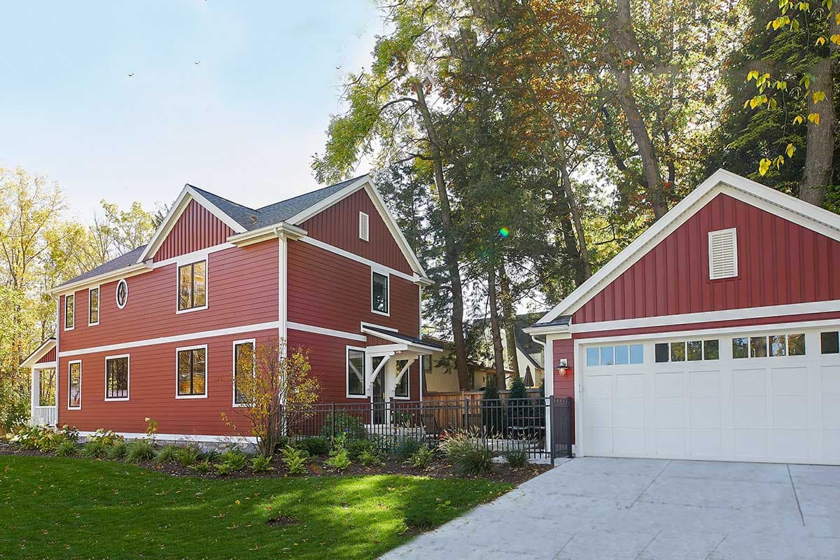 Two-story red house plan with white trim, gables, dormers, and attached garage. Features include a covered entryway and fenced yard.