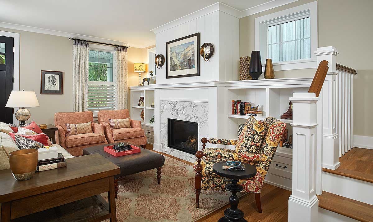 Living room with marble fireplace, built-in shelving, two orange armchairs, and a patterned armchair.