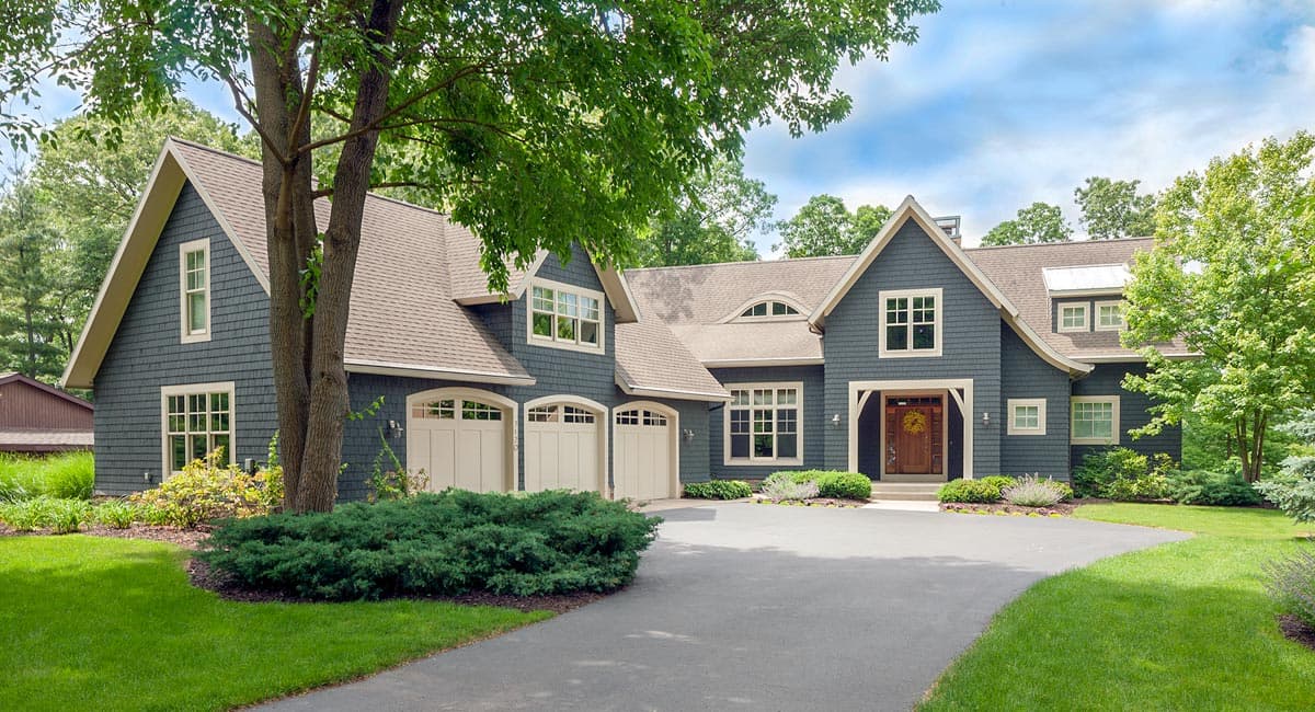 House plan exterior. Craftsman style, two-story home with gabled roof, dormers, and attached garage. A tree and landscaped lawn are in the foreground.