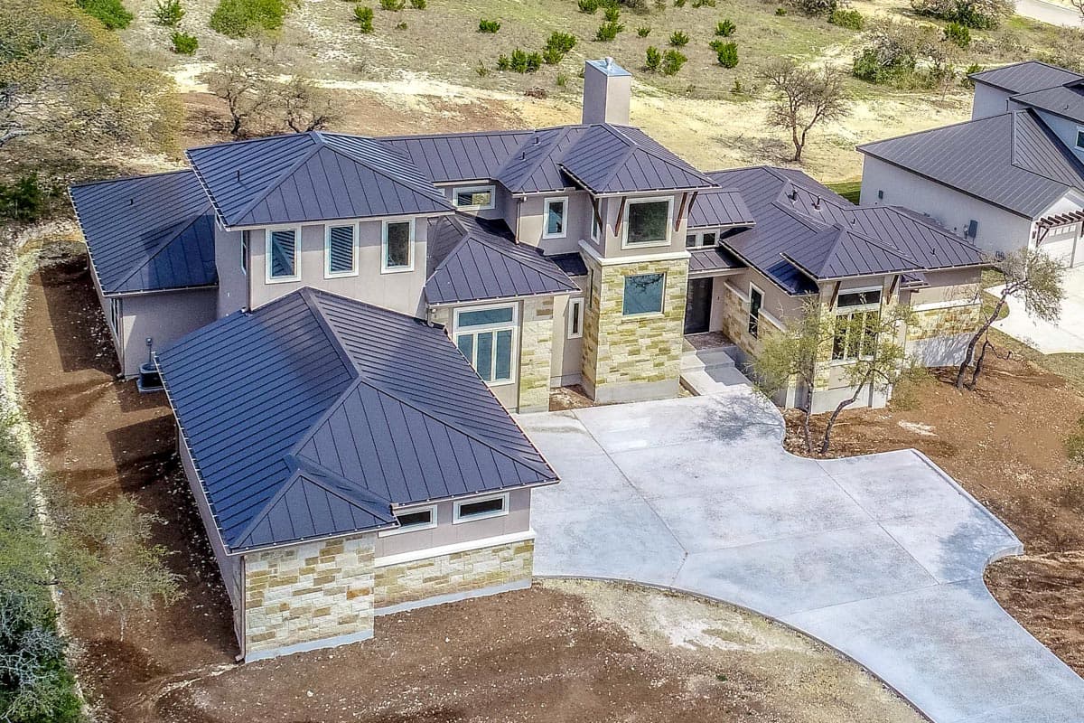 House plan exterior featuring a multi-story design with metal gables, stone accents, and a prominent chimney.