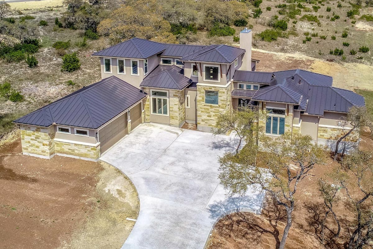 House plan exterior, two-story, with stacked stone accents, metal roof, and attached three-car garage.