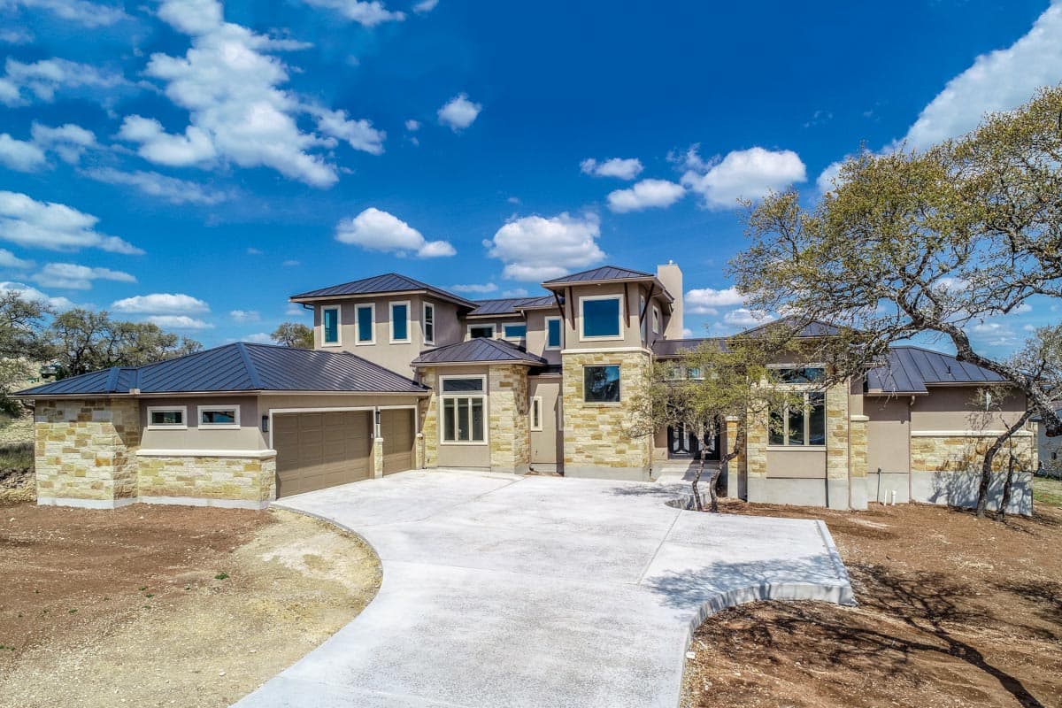 House plan exterior. Two-story, contemporary design with multiple rooflines, stone and stucco facade, and attached garage with a metal roof.
