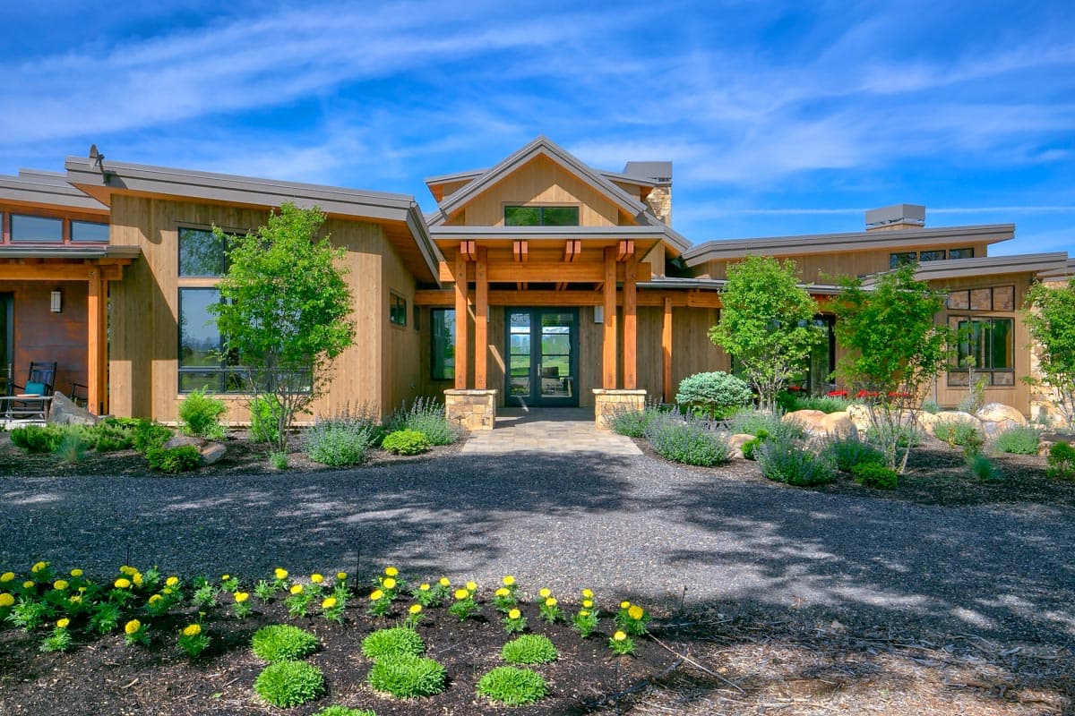Modern house plan exterior with wood siding, gabled rooflines, covered entrance with exposed beams, and large windows.