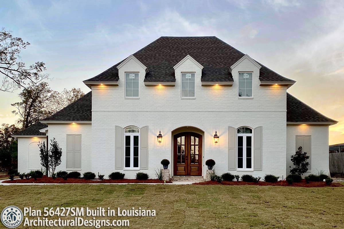 House plan exterior: two-story brick home with hipped roof, dormers, arched entry, and shutters.