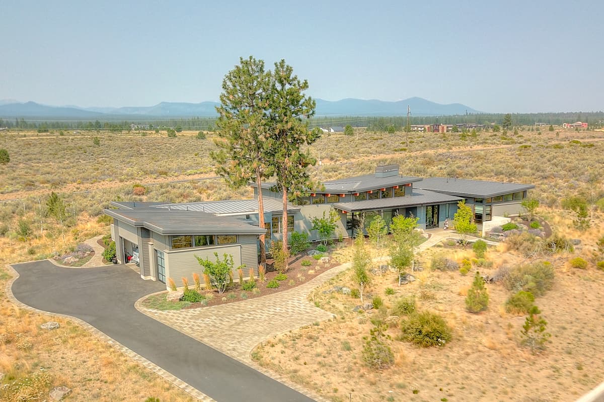 Modern single-story house plan exterior with a flat roof, large windows, and attached garage. Features a curving driveway and stone paver walkway.