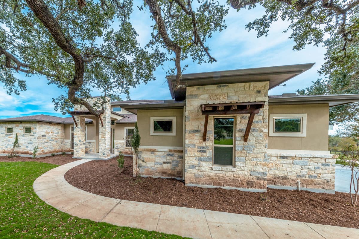 House plan exterior with stone accents, flat roofline, covered entry with stone pillars, and multiple windows.