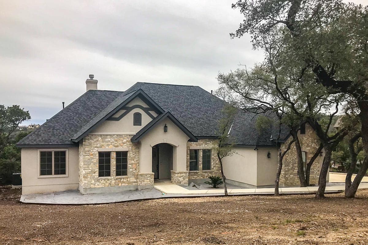 House plan exterior: One-story home with stone accents, arched entry, and dark asphalt shingle roof.