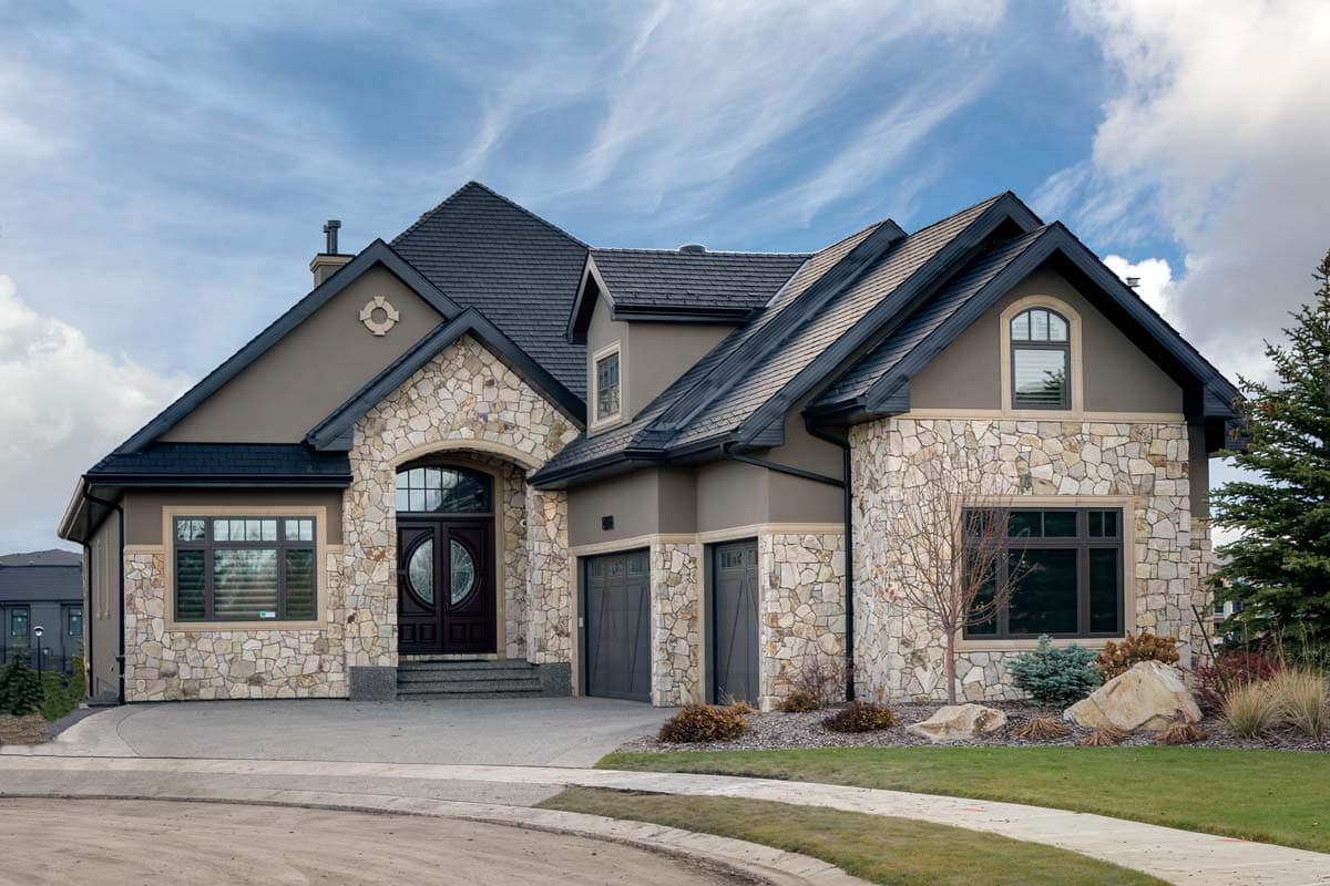 House plan exterior featuring stone facade, multiple gables, arched entry, and a two-car garage. Two story home with dark trim and roof.