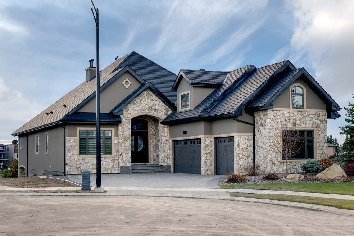 House plan exterior showing stone accents, arched entryway, multiple gables, and a three-car garage.