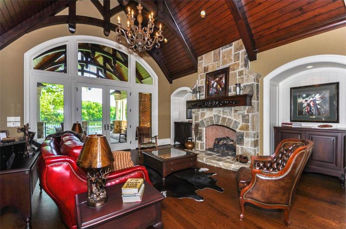 Interior rendering of a great room with vaulted wood-beamed ceiling, stone fireplace, and large arched windows.