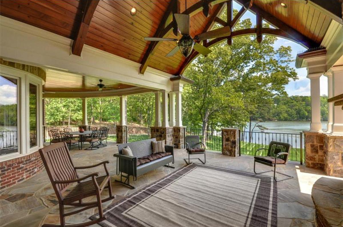 Covered outdoor living space with wood ceiling, fans, stone columns, seating, dining area, and lake view.