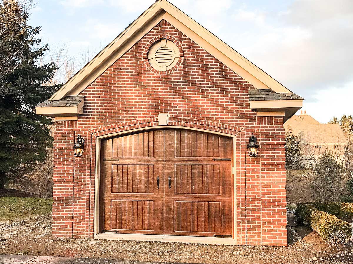 Brick garage with arched wooden doors, gable roof, and decorative circular vent.