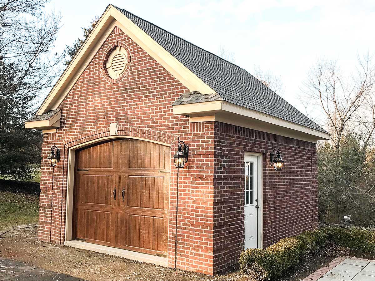 House plan exterior: brick garage with arched wooden double door, side entry door, circular gable vent, and pendant lighting.