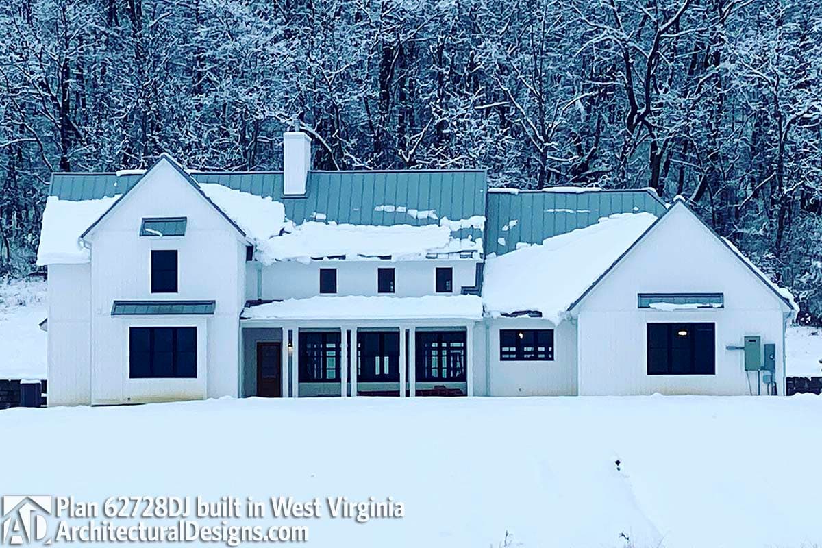 Modern farmhouse exterior with white board and batten siding, metal roof, gables, and covered porch with square columns.