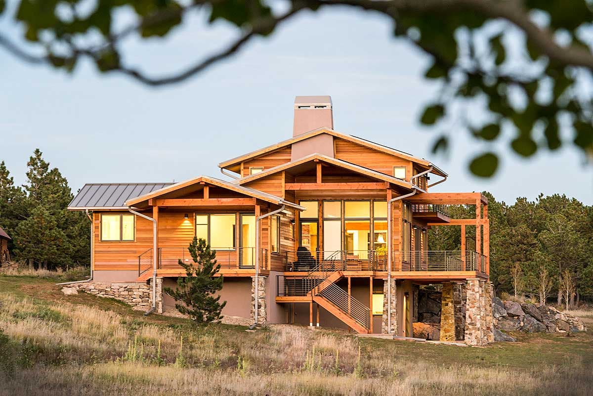 Modern house plan exterior with wood siding, metal roof, large windows, multiple decks, and stone foundation.