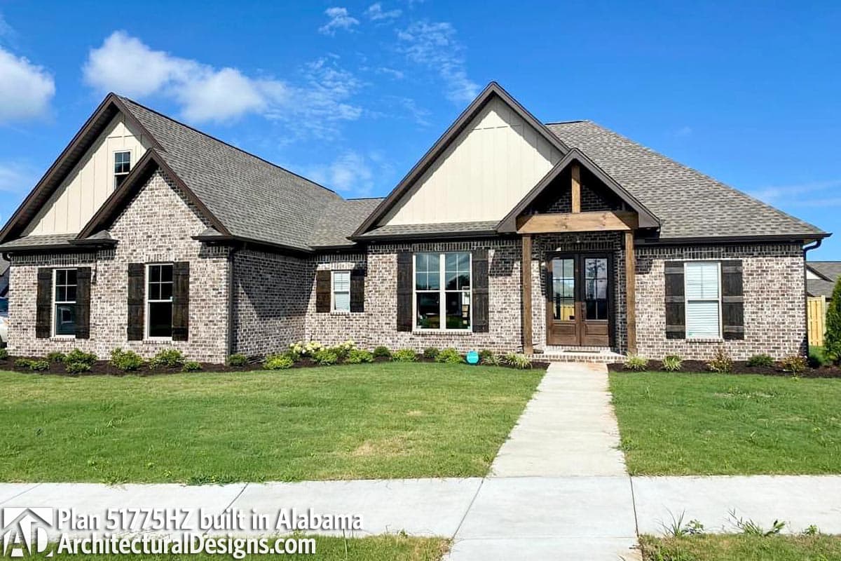 House plan exterior: One-story brick home with gables, dormers, a covered entry with wood beams, and dark shutters.
