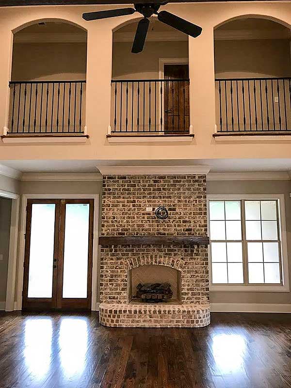 Interior view showing a brick fireplace, wood floors, double doors, and a loft with arched openings and wrought iron railings.