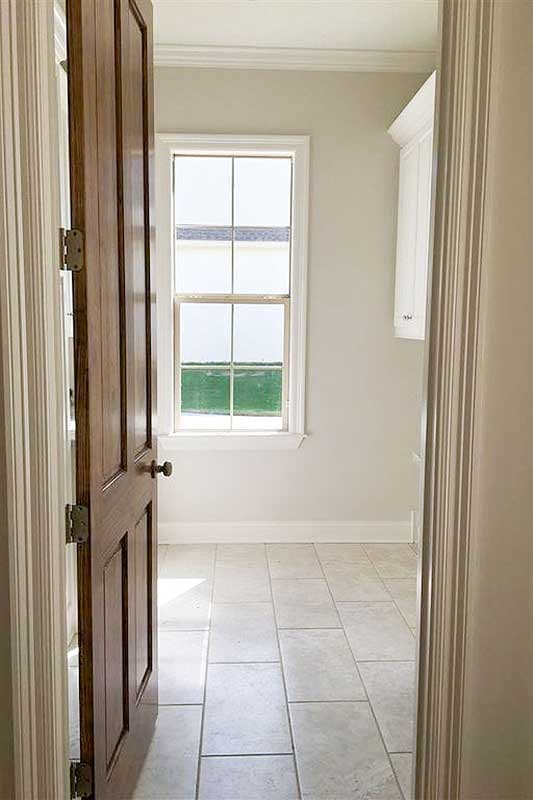 Interior view showing a wood door opening into a room with tiled floor, single-hung window, and cabinetry.
