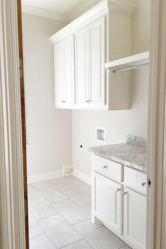 Laundry room with white shaker cabinets, granite countertop, tile flooring, and hookups.